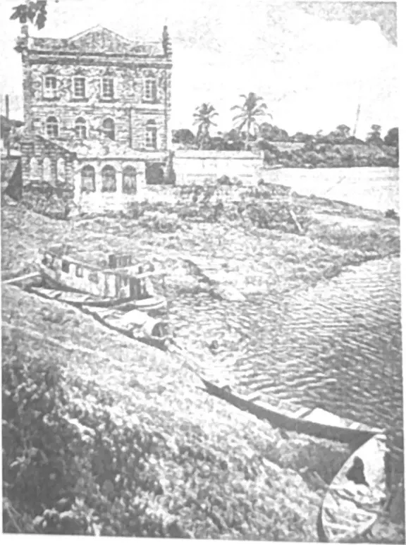 Fotografia antiga em preto e branco, com retícula de impressão, de um sobrado no alto do barranco e barcos atracados na margem