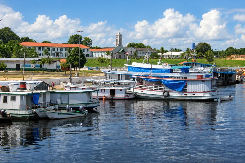 Imagem colorida de barcos regionais de dois andares atracados no porto de Tefé, com o antigo Seminário São José e a torre da catedral ao fundo